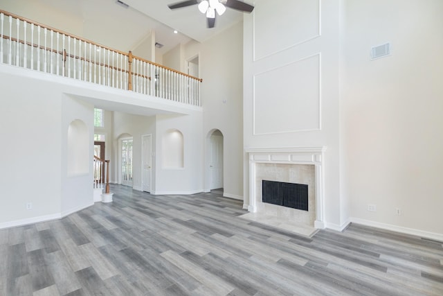 unfurnished living room with ceiling fan, visible vents, arched walkways, wood finished floors, and a high ceiling