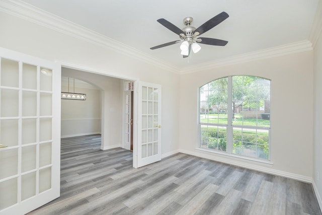 empty room with baseboards, ornamental molding, arched walkways, and wood finished floors