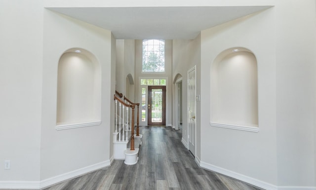 entrance foyer featuring stairs, arched walkways, baseboards, and wood finished floors