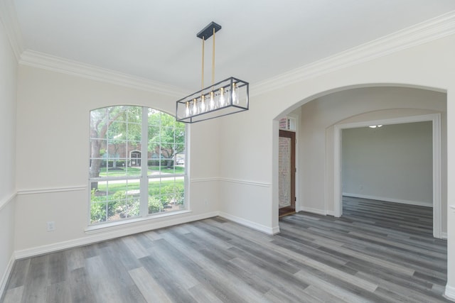 unfurnished dining area featuring crown molding, arched walkways, wood finished floors, and a notable chandelier