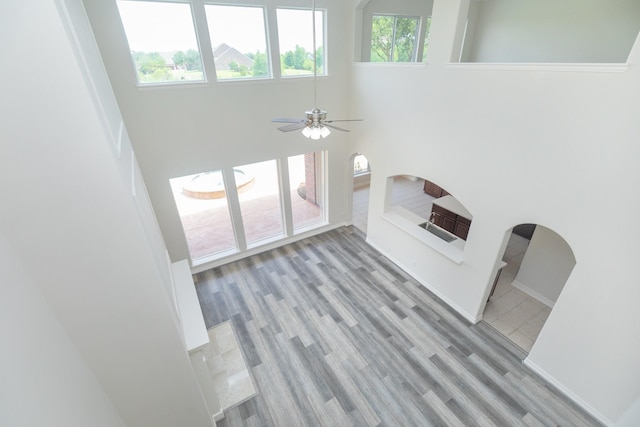 unfurnished living room with baseboards, a ceiling fan, a high ceiling, and wood finished floors