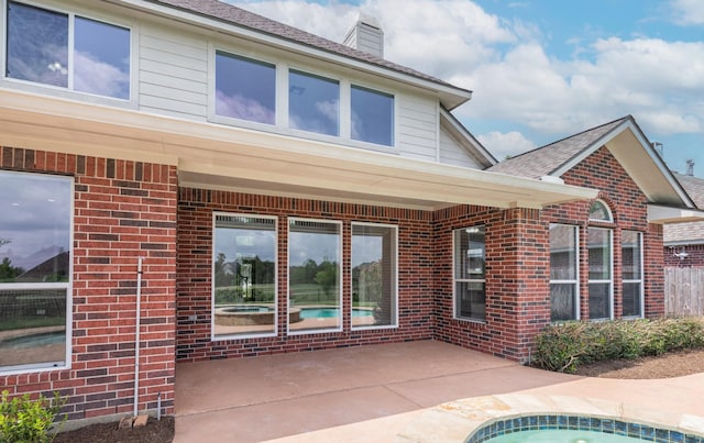back of property featuring brick siding, a chimney, a shingled roof, and a patio area