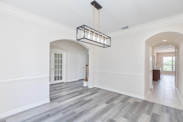 unfurnished dining area with visible vents, ornamental molding, baseboards, arched walkways, and light wood-style flooring