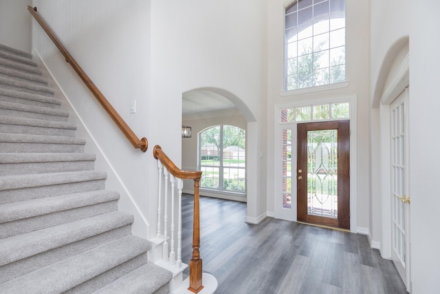 foyer with wood finished floors, baseboards, a high ceiling, stairway, and arched walkways