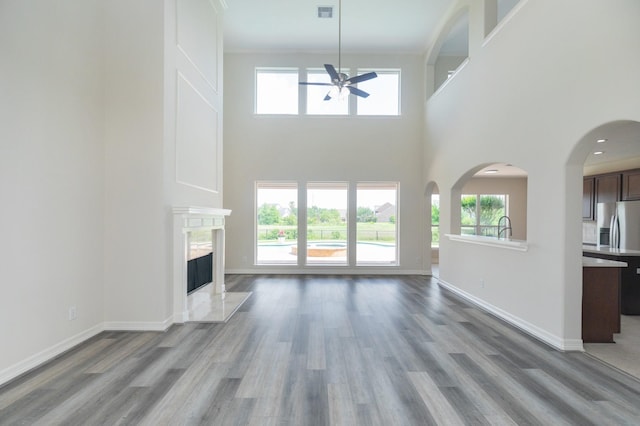 unfurnished living room featuring ceiling fan, visible vents, a fireplace, wood finished floors, and a high ceiling