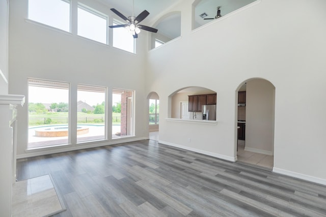 unfurnished living room with baseboards, a towering ceiling, ceiling fan, and wood finished floors