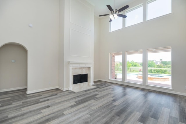 unfurnished living room featuring a healthy amount of sunlight, a ceiling fan, a towering ceiling, a fireplace, and baseboards