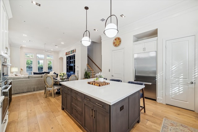kitchen featuring dark brown cabinetry, crown molding, appliances with stainless steel finishes, pendant lighting, and white cabinetry