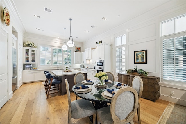 dining area featuring visible vents, light wood-style flooring, and crown molding