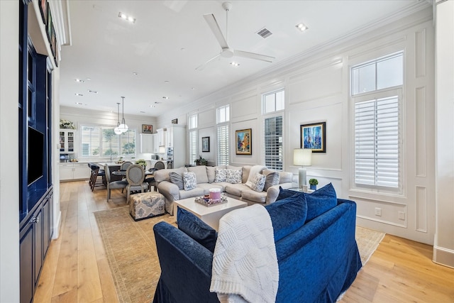 living room with crown molding, light wood-style floors, and visible vents