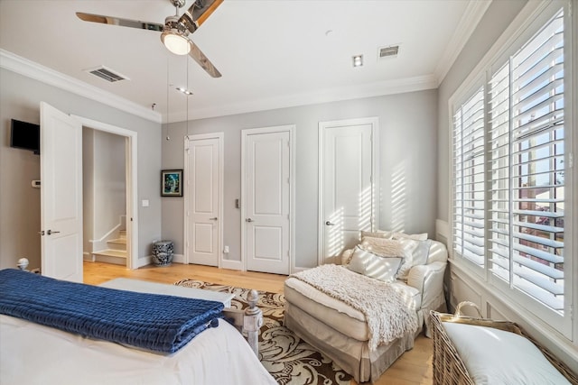 bedroom featuring two closets, visible vents, ornamental molding, and light wood finished floors