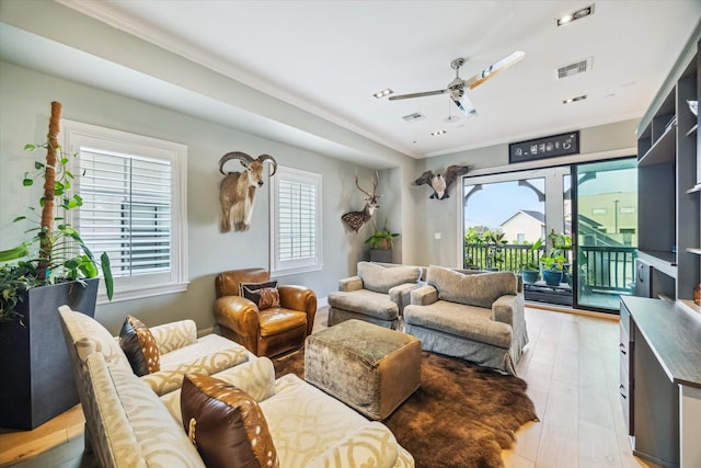 living room with visible vents, ornamental molding, light wood-style floors, and ceiling fan