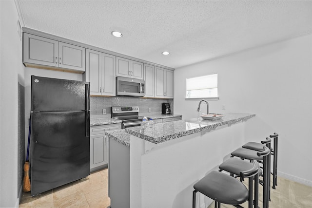 kitchen featuring a breakfast bar area, stainless steel appliances, recessed lighting, and gray cabinets