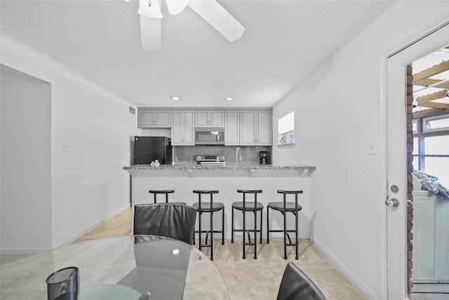 kitchen with a peninsula, a breakfast bar, light stone counters, appliances with stainless steel finishes, and backsplash