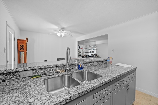 kitchen featuring light stone counters, a sink, gray cabinets, a ceiling fan, and baseboards