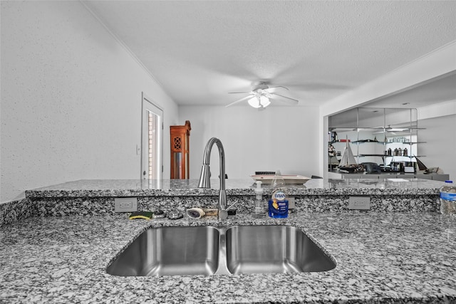 kitchen with a sink, stone counters, ceiling fan, and a textured ceiling