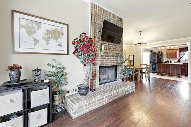 living room with crown molding, a notable chandelier, dark wood finished floors, and a brick fireplace