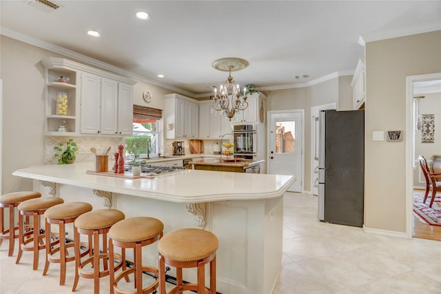 kitchen featuring light countertops, freestanding refrigerator, a peninsula, decorative backsplash, and visible vents