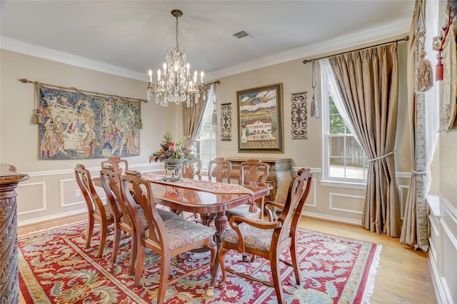 dining space featuring visible vents, ornamental molding, a decorative wall, light wood-type flooring, and a notable chandelier