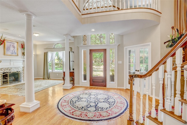 foyer entrance with a fireplace with flush hearth, a high ceiling, ornate columns, and wood finished floors