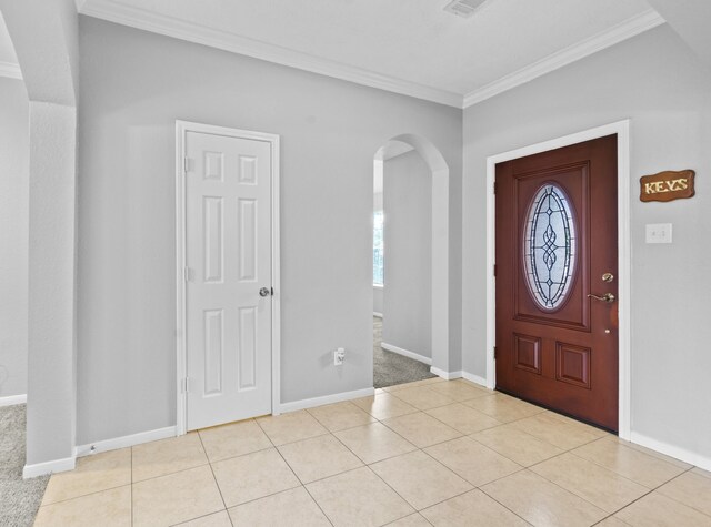 foyer entrance with crown molding, arched walkways, baseboards, and plenty of natural light