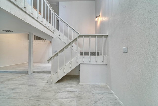 stairway featuring baseboards, marble finish floor, and a textured wall