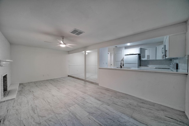 unfurnished living room with a sink, a brick fireplace, marble finish floor, a ceiling fan, and visible vents