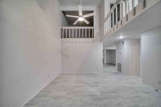 unfurnished living room with a ceiling fan, visible vents, a towering ceiling, baseboards, and marble finish floor