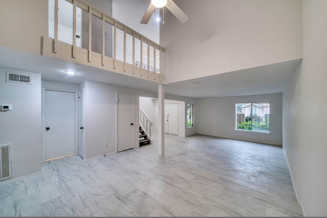 unfurnished living room with visible vents, stairs, baseboards, a high ceiling, and a ceiling fan