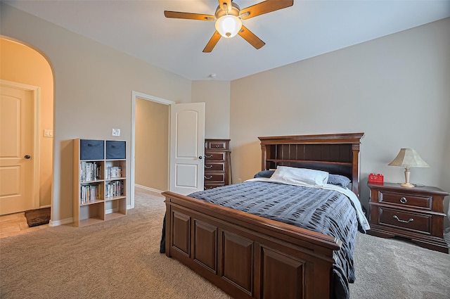 bedroom with light colored carpet, arched walkways, baseboards, and ceiling fan
