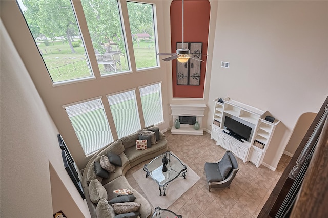 living room with light tile patterned floors, a high ceiling, a ceiling fan, and a glass covered fireplace