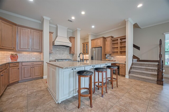 90 Wyndehaven Lakes Dr, Katy, TX 77494 - kitchen featuring stainless steel fridge, open shelves, premium range hood, a kitchen island with sink, and light stone counters