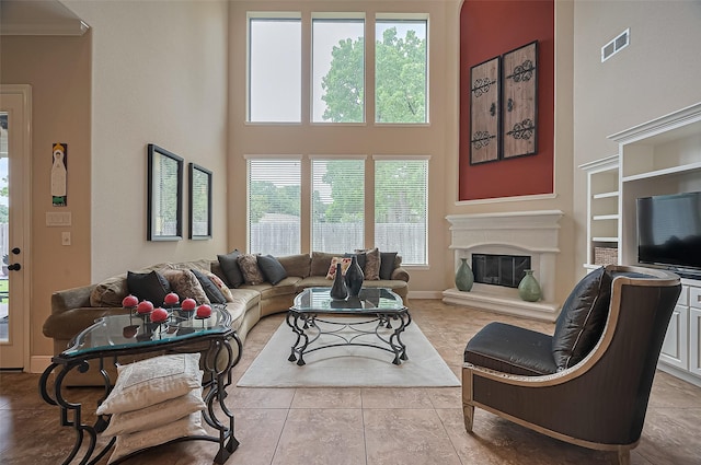 living room with visible vents, tile patterned flooring, a glass covered fireplace, a towering ceiling, and built in shelves