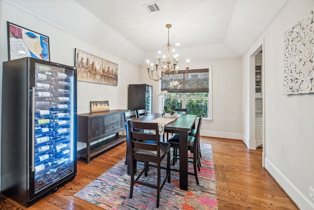 dining area with visible vents, wood finished floors, baseboards, a raised ceiling, and a chandelier