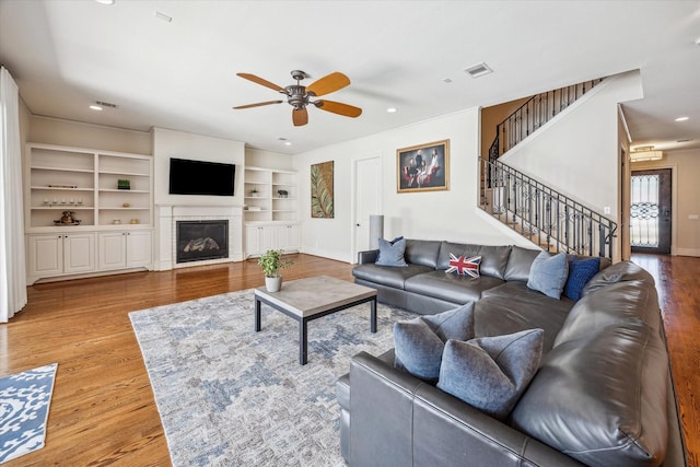 living room with built in shelves, ceiling fan, stairs, and wood finished floors