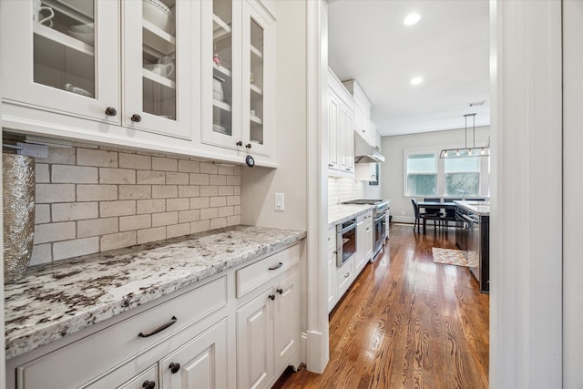 kitchen with glass insert cabinets, dark wood-style floors, white cabinetry, under cabinet range hood, and light stone counters