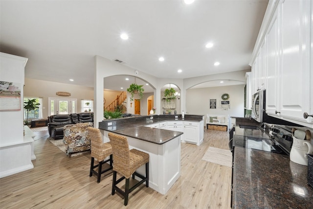 kitchen featuring a breakfast bar area, arched walkways, white cabinets, open floor plan, and recessed lighting