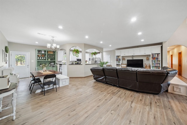 living area featuring arched walkways, a notable chandelier, visible vents, and light wood finished floors