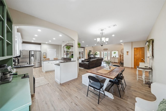 kitchen with stainless steel fridge, arched walkways, light wood-style flooring, and white cabinets