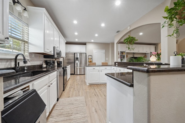 kitchen with appliances with stainless steel finishes, a sink, light wood finished floors, recessed lighting, and white cabinetry