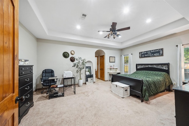 bedroom featuring ceiling fan, visible vents, arched walkways, a tray ceiling, and carpet flooring