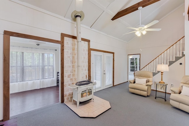 carpeted living area with ceiling fan, a wood stove, high vaulted ceiling, stairs, and beamed ceiling