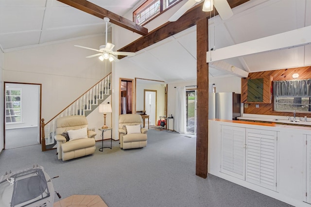 carpeted living area with a ceiling fan, a sink, and beam ceiling