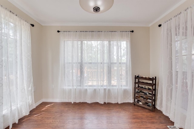 unfurnished room with crown molding, dark wood-style flooring, and baseboards