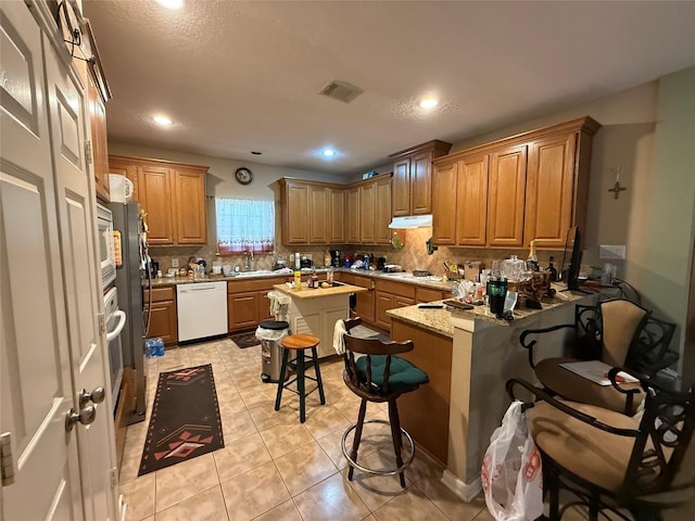8813 Lauren Ln, Waller, TX 77484 - kitchen featuring visible vents, decorative backsplash, a breakfast bar, white dishwasher, and under cabinet range hood
