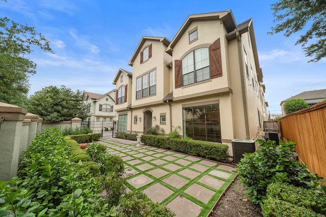 rear view of property featuring a gate, central AC unit, stucco siding, and fence private yard