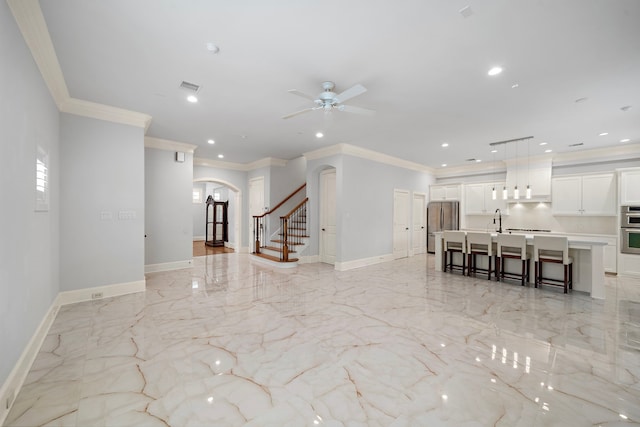 unfurnished living room featuring crown molding, a sink, arched walkways, baseboards, and stairway