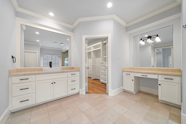 bathroom with crown molding, a walk in closet, a sink, recessed lighting, and two vanities