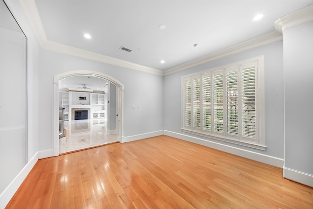 unfurnished living room featuring crown molding, arched walkways, baseboards, and light wood-type flooring