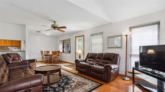 living area with a textured ceiling, baseboards, ceiling fan, and light wood-type flooring